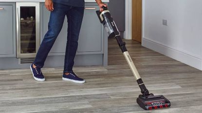 A person using a cordless vacuum in their kitchen from Shark Clean.