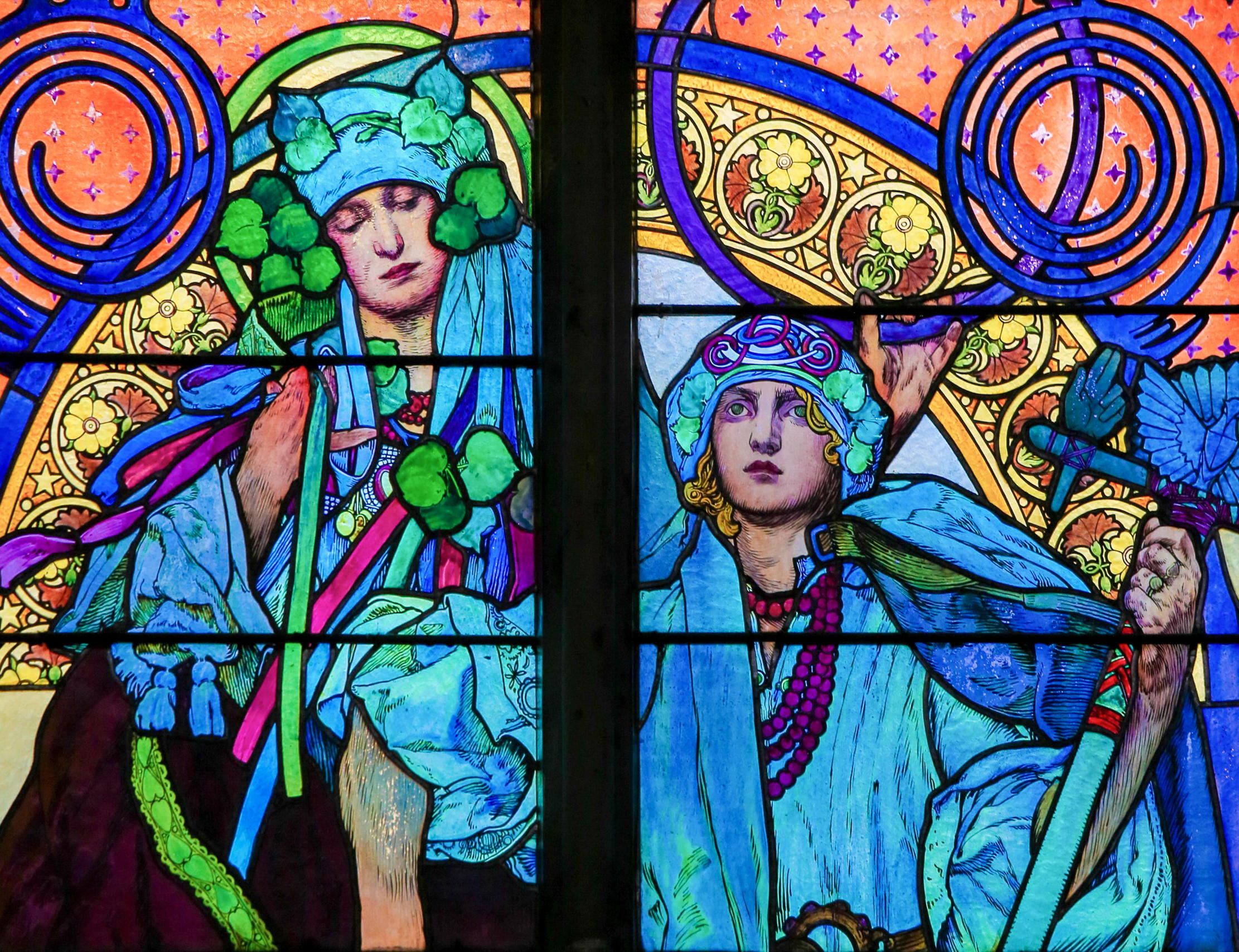 A stained glass window by Mucha, showing two women in blue