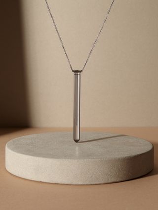 Neutral base and background, circular beige stone plinth in centre, displaying a silver chain clear pendant necklace