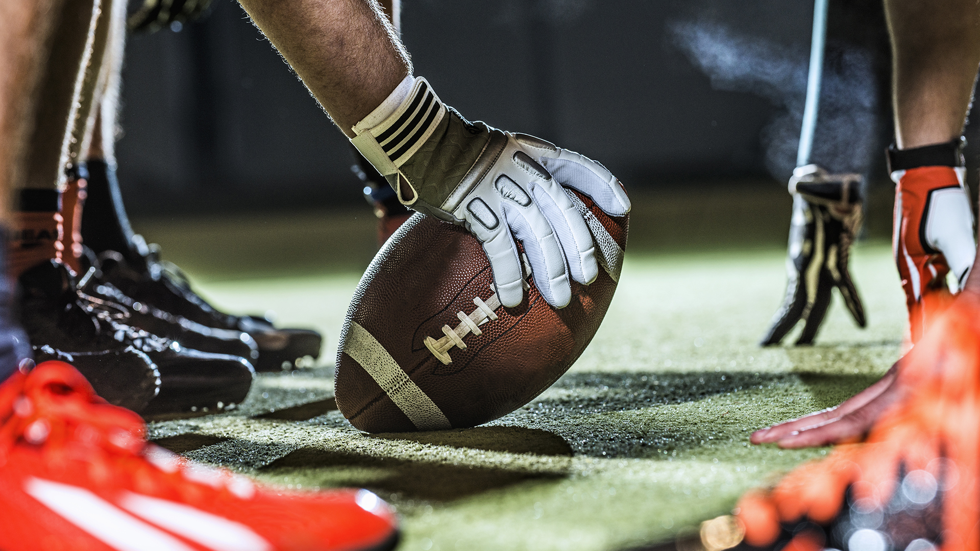 A close up of an American football on the field held in gloved hands