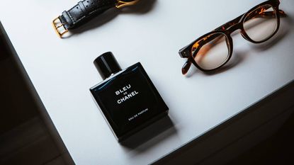 Chanel fragrance bottle lying on a table next to glasses and a watch