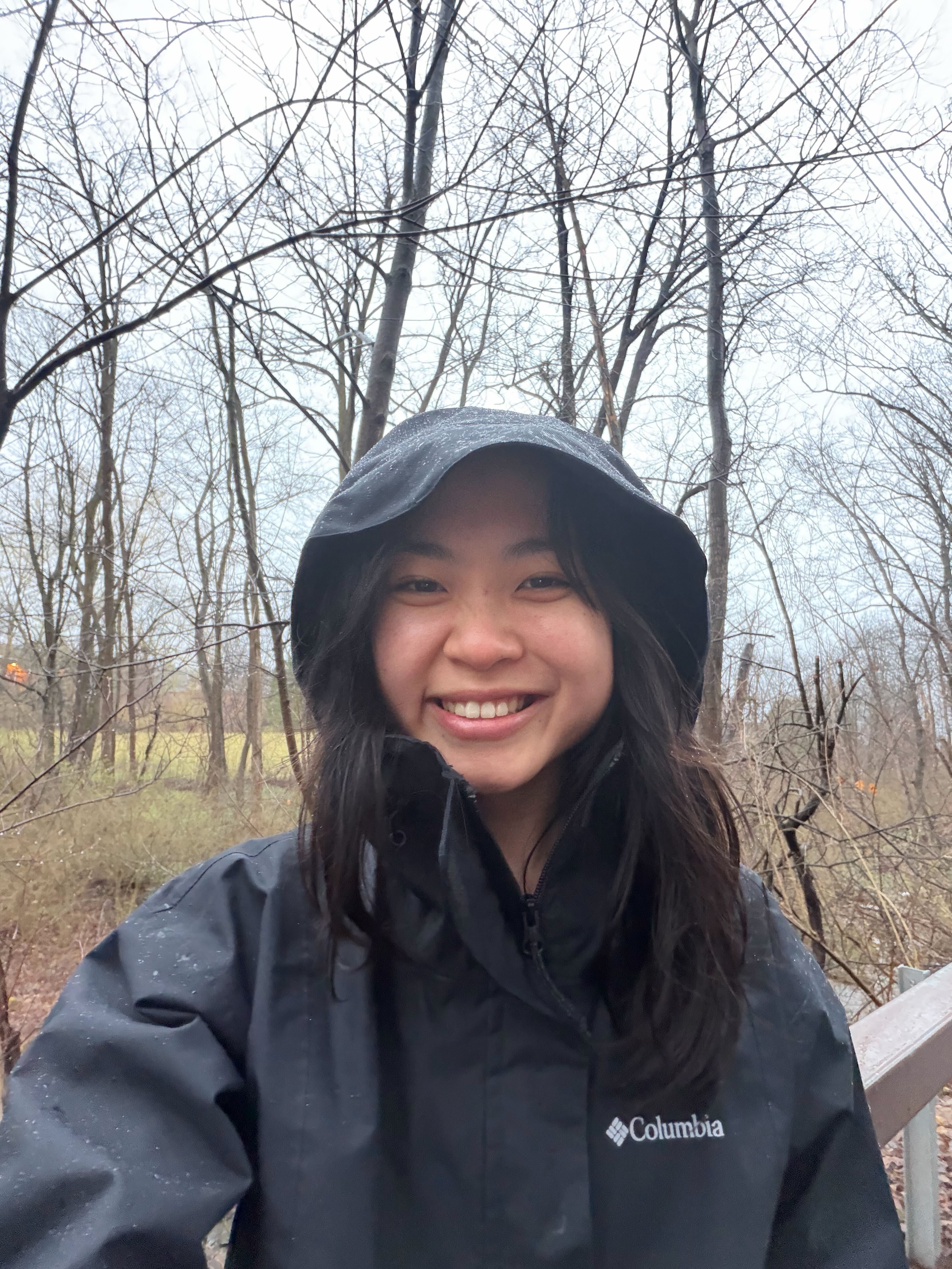 young woman wearing black anorak in a field with trees