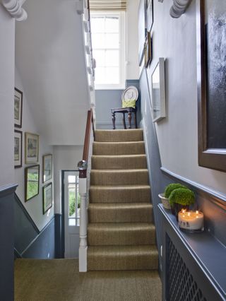 Landing with flight of stairs below and above and natural floorcovering and grey wall below dado and white wall above