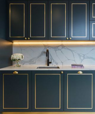 blue green dark teal kitchen with marble backsplash and gold molding on cabinet fronts