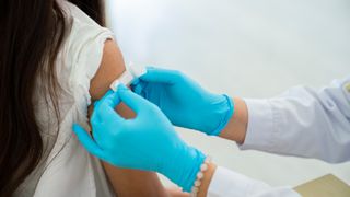 Gloved doctor applies bandage to girl's arm following an immunization.