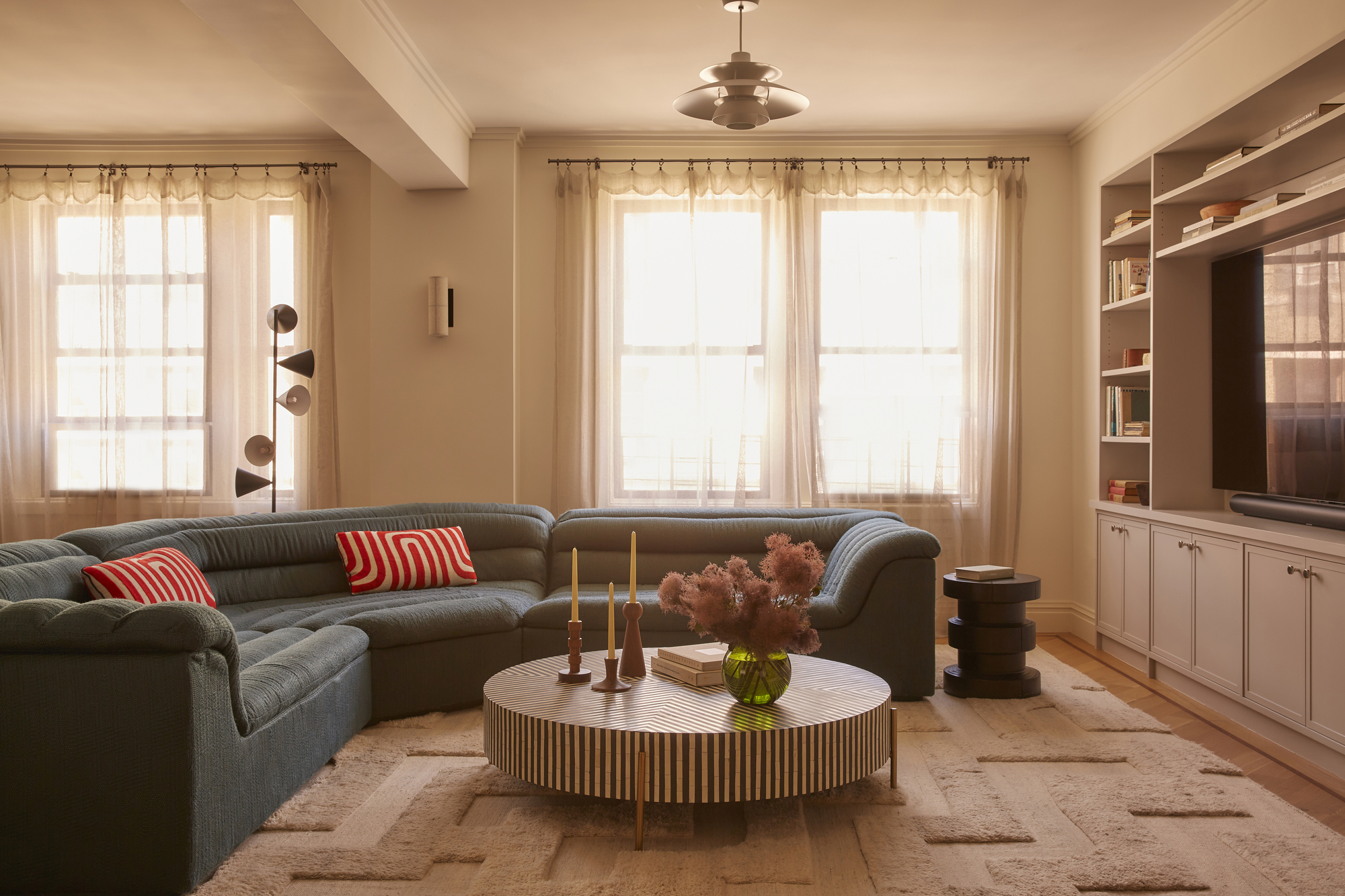 modern living room with navy blue L-shaped sofa with round striped coffee table with cabinetry with TV in it