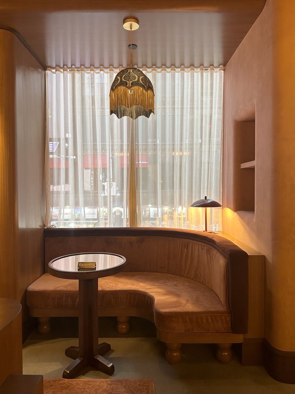 Cozy corner booth at Charlie Fox, on Times Square. Softly lit, peach toned sitting area.
