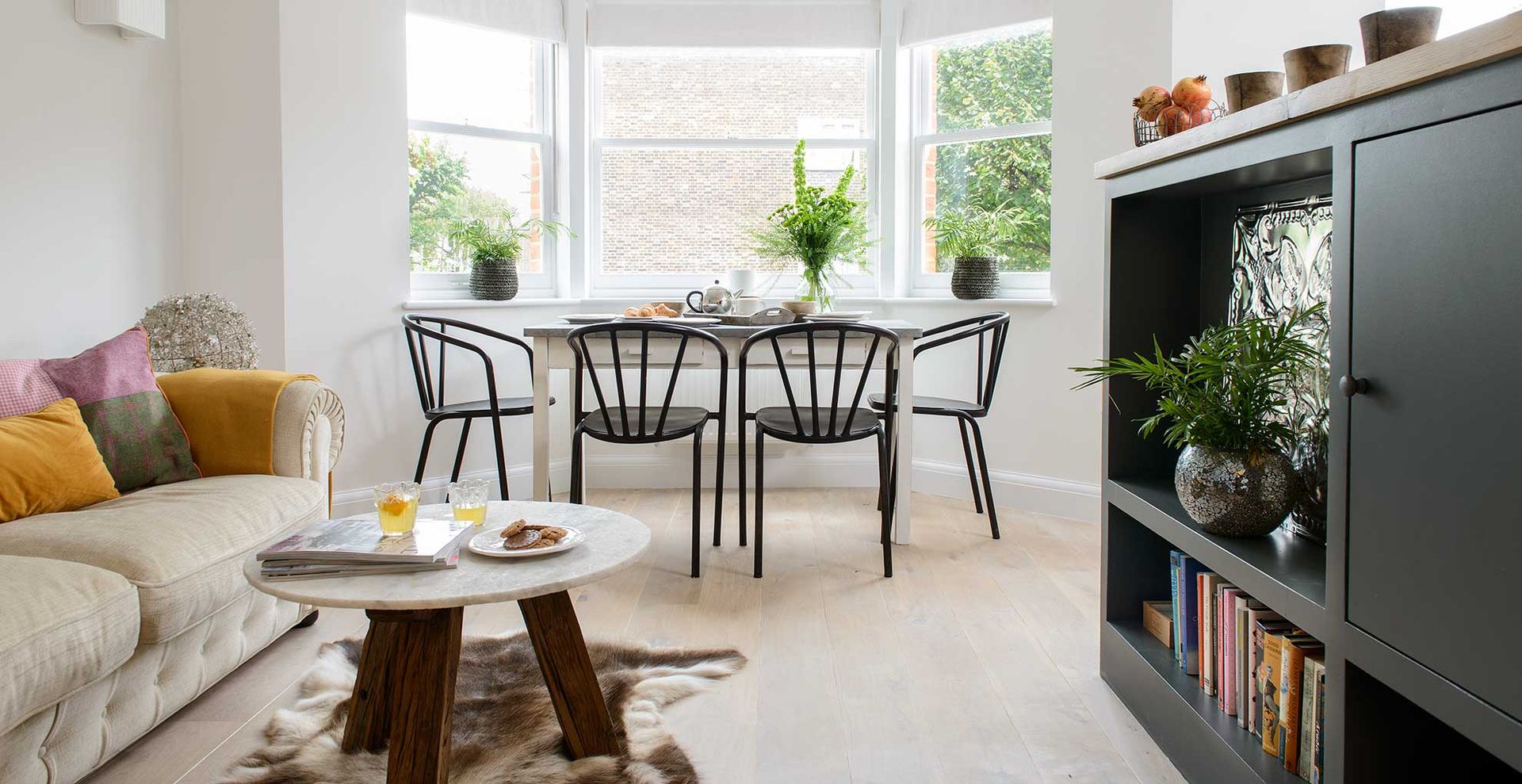white living room with large bay window with dining table, brown leather sofa and black wall unit with tv and book storage to show how to declutter a living room