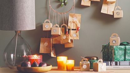 A sideboard decorated with candles, a bowl of figs and an alternative advent calendar made from little paper bags and boxes