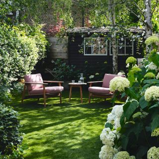 Seating area in the garden surrounded by trees and flowerbeds with white and green hydrangeas. Interior designer Susan Hoodless and Erskine Berry's renovated four storey terraced west London home.