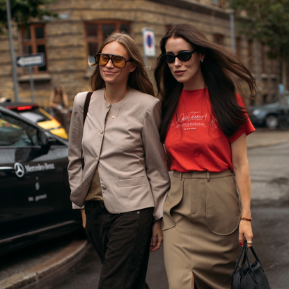 woman wearing a tan blazer and jeans next to a woma in a red tee and a brown skirt 