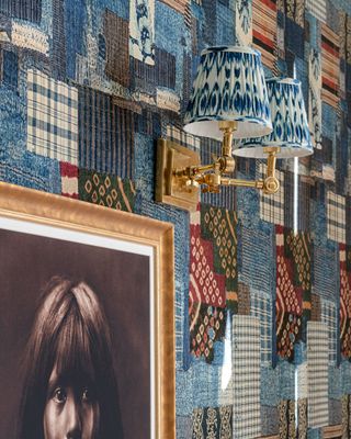 A painting on a colourful wallpapered wall with a wall sconce above