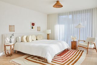 A bedroom with white walls, white bedding, and orange carpet and jute light