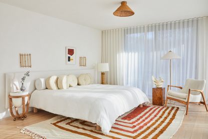 A bedroom with white walls, white bedding, and orange carpet and jute light 