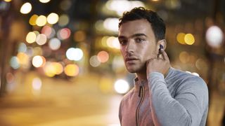 A man waiting to cross a busy street and activating the Jabra Elite 4 Active's HearThrough mode.