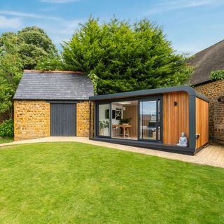 Green Retreats garden room with wooden and black exterior next to brick storage shed