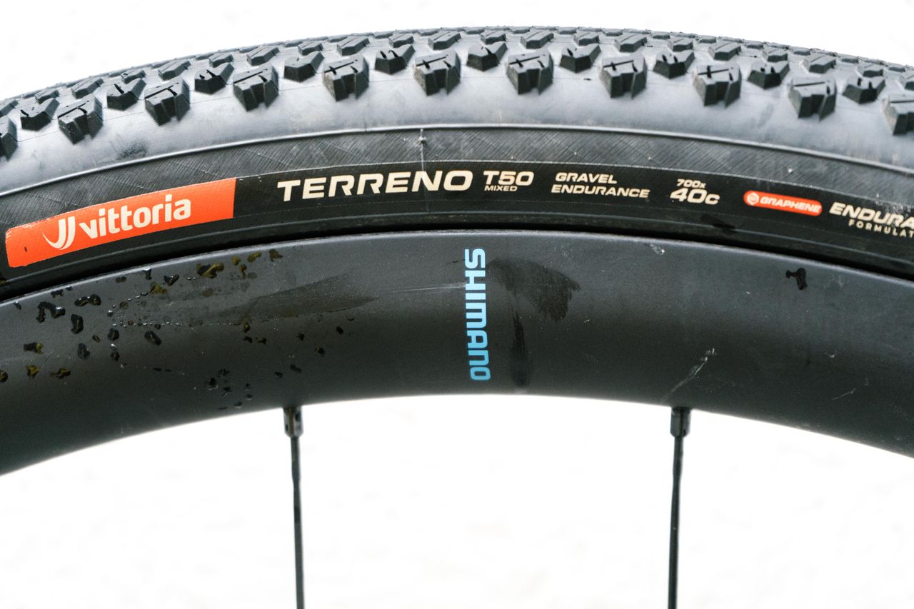 The rear wheel of a gravel bike against a white wall