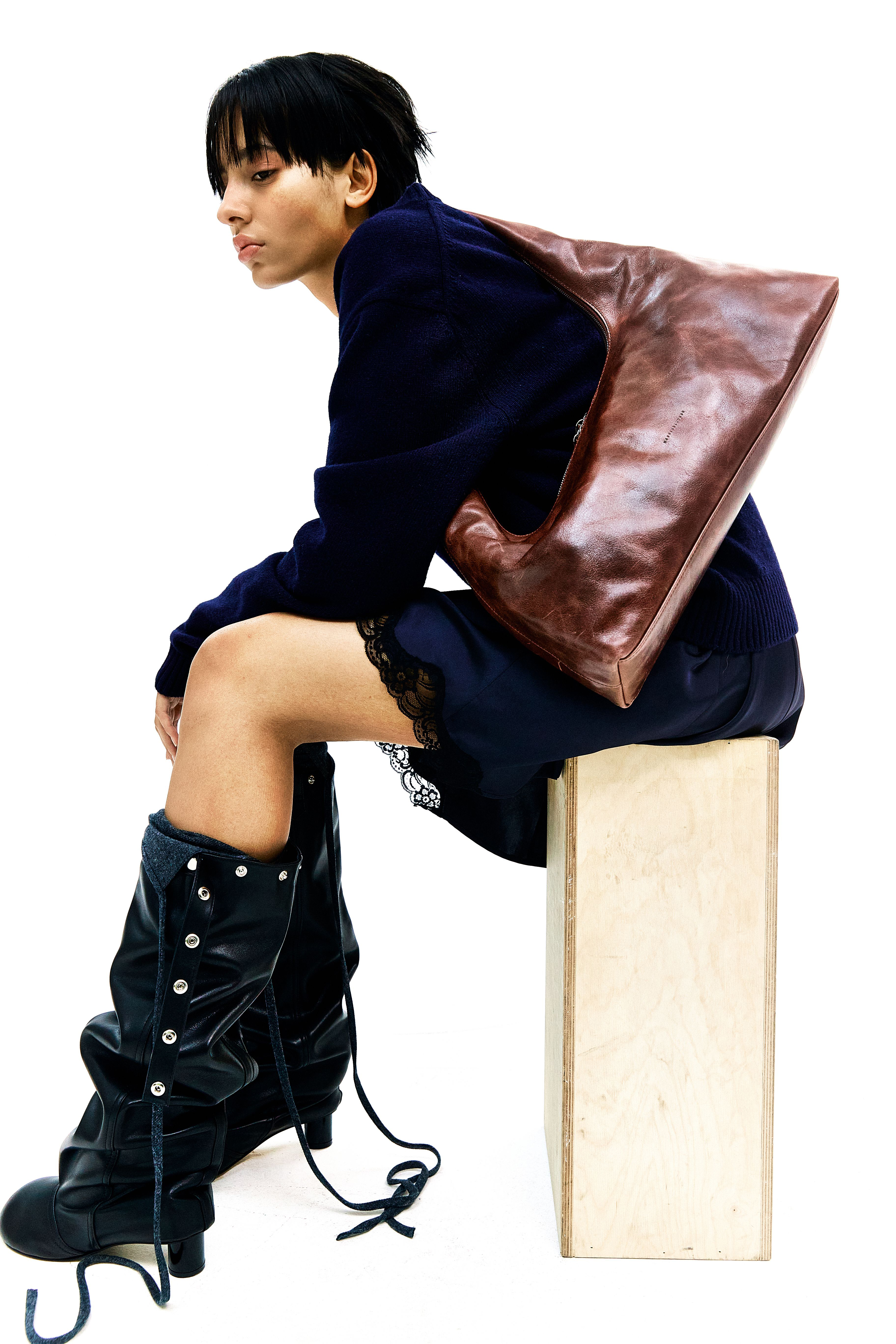 a woman wearing a brown shoulder bag, black dress, and black boots