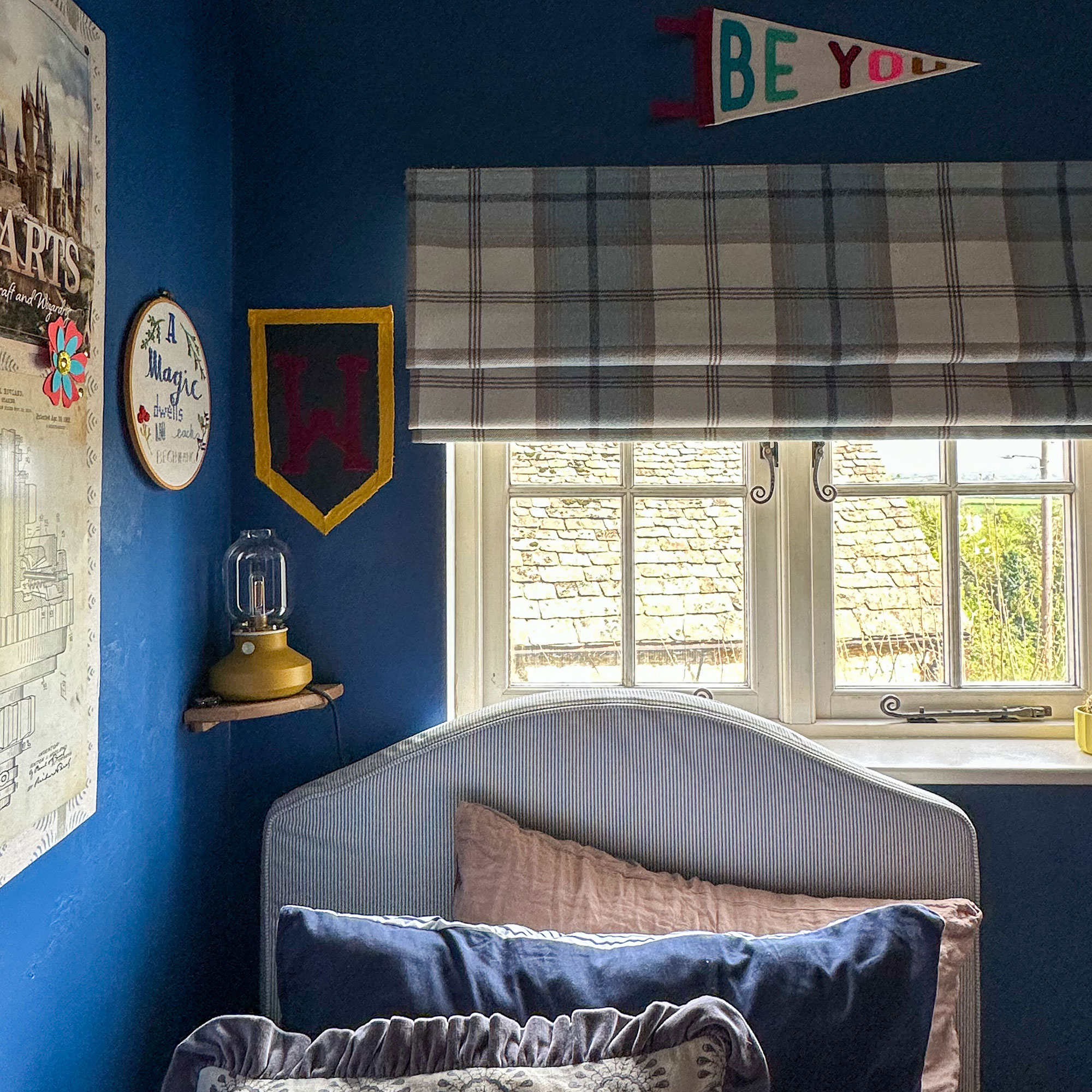 Blue boy's bedroom with striped upholstered headboard on twin bed, tartan window blinds and colourful wall decor