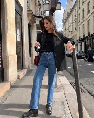 Influencer Leasy in Paris wearing black t-shirt, black blazer, and straight-leg mid-wash denim jeans while standing in Paris street.