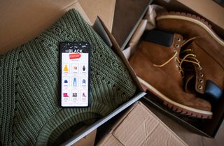 A jumper and a pair of boots in boxes with a phone displaying Black Friday deals.