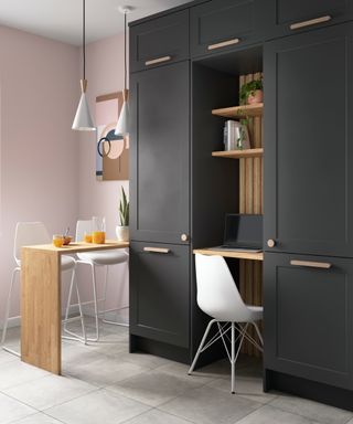 kitchen with small desk space fitting between two floor to ceiling dark grey cabinets with wooden breakfast bar to one side with white stools