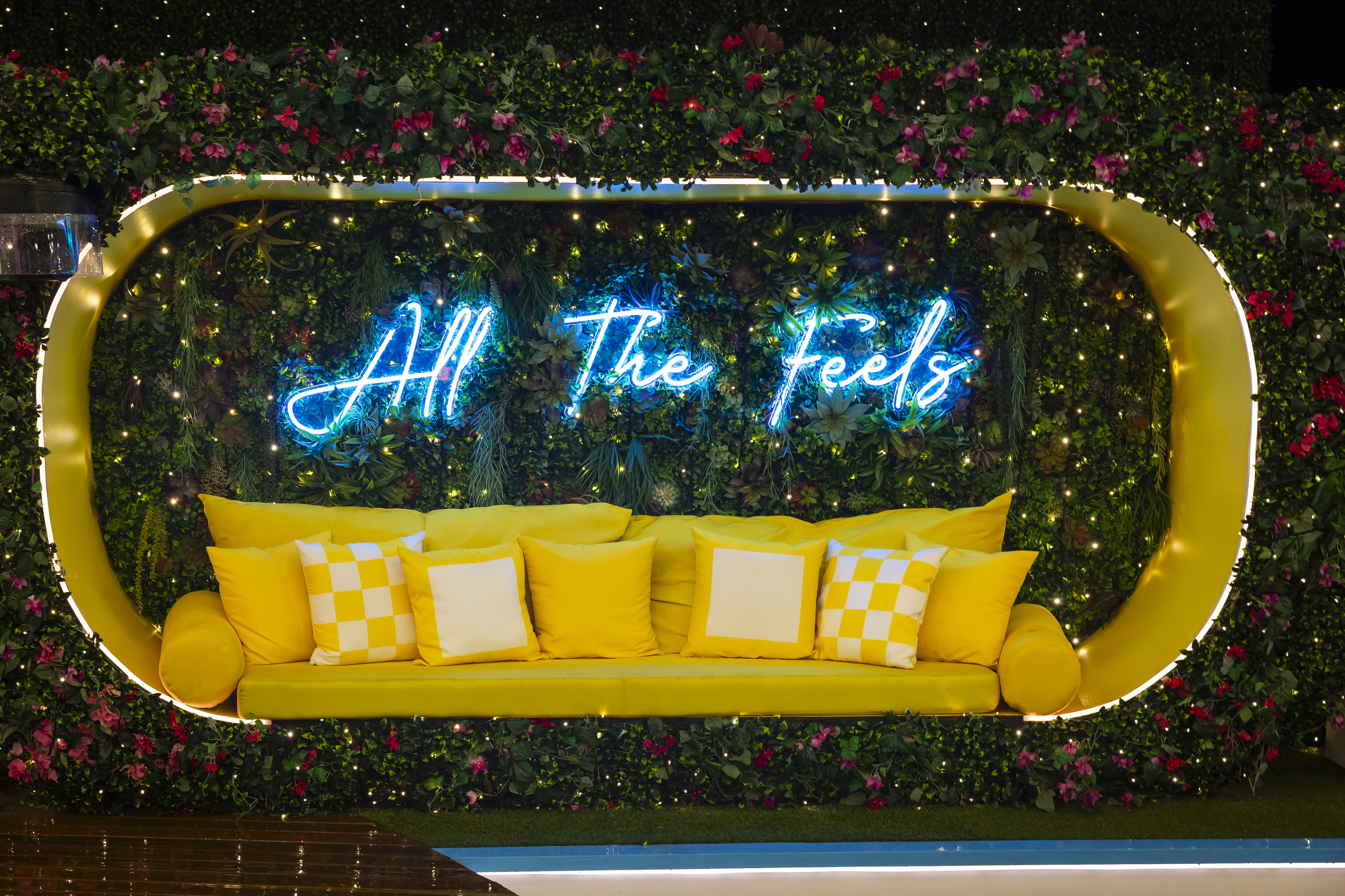 A yellow bench sunk into a wall covered with flowers, with a neon sign reading &amp;quot;All the Feels,&amp;quot; in the 'Love Island USA' season 7 villa.