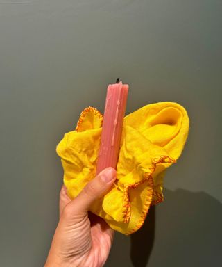 Person holding pink candle and yellow cloth on green background