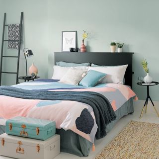 Green bedroom with black headboard and ladder shelving and pastel trunk storage
