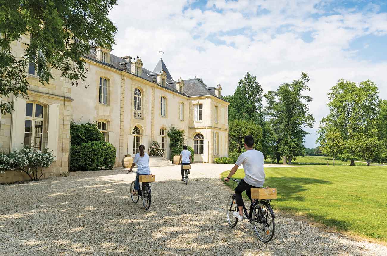 Three people on bicycles approaching Ch&amp;acirc;teau de Reignac in Entre-deux-Mers