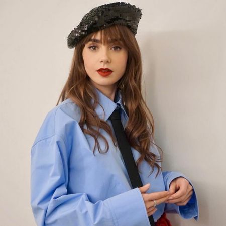 Lily Collins wearing a sequin beret with a Valentino blue shirt and black tie doing press for Emily In Paris season 4.