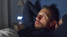 Man lying bed with hands behind his head, eyes open