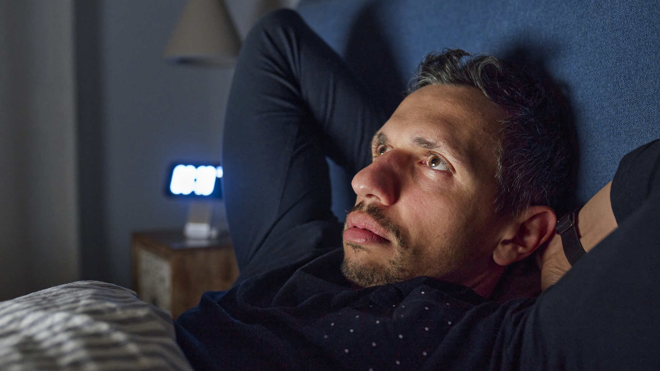 Man lying bed with hands behind his head, eyes open