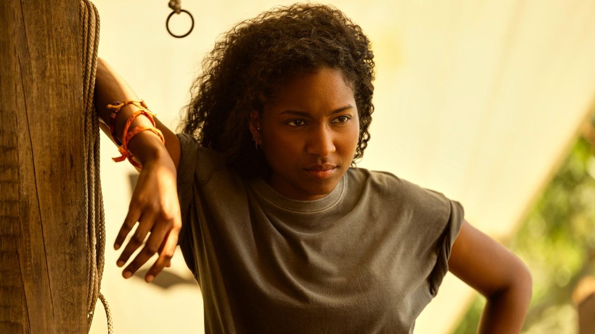 Carlacia Grant as Cleo looking motivated with her left arm resting on a post. 