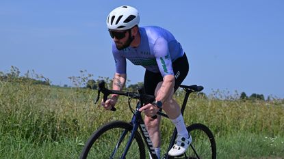 Tech Editor Andy Carr riding one the best budget road bikes the Giant Contend SL 1 alongside one of the best budget helmets the Van Rysel RCR Mips. All to the backdrop of a tall grass verge. 