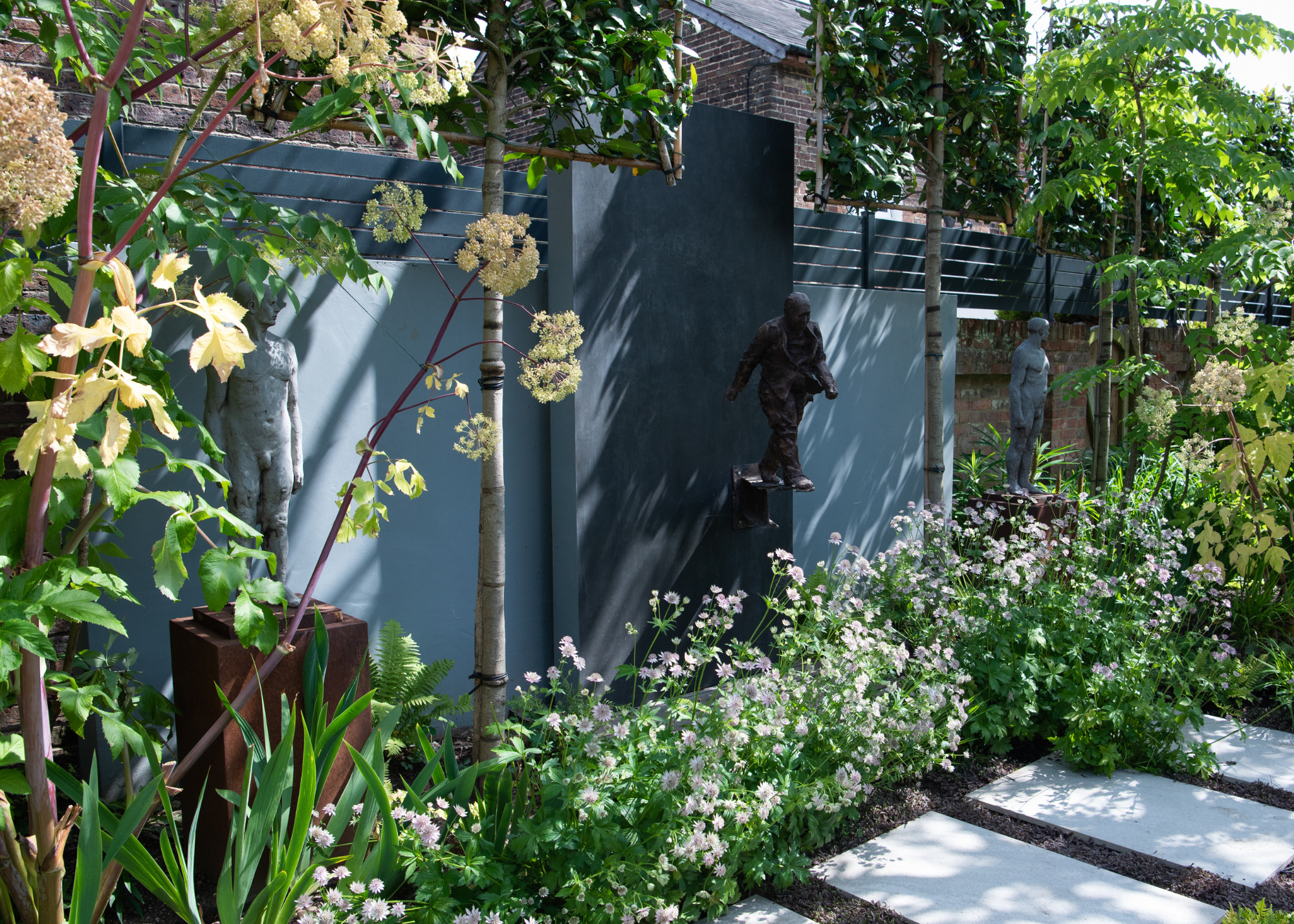 three small full-body bronze sculptures on plinths lining the edge of a garden design