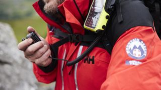 A close-up of the Helly Hansen jacket of a mountain rescue volunteer, showing the radio clipped to his chest.