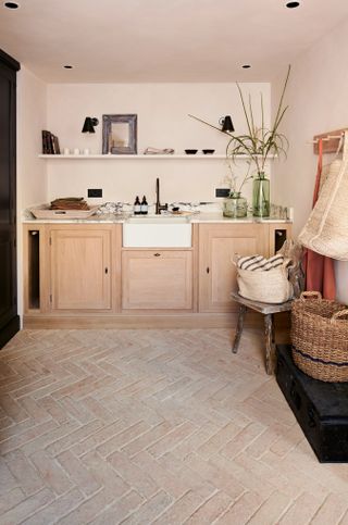 A small neutral kitchen with a Belfast sink and herringbone terracotta floor tiles