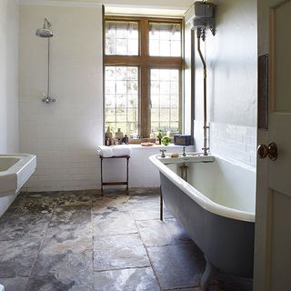 bathroom with white wall bathtub window and stone flooring