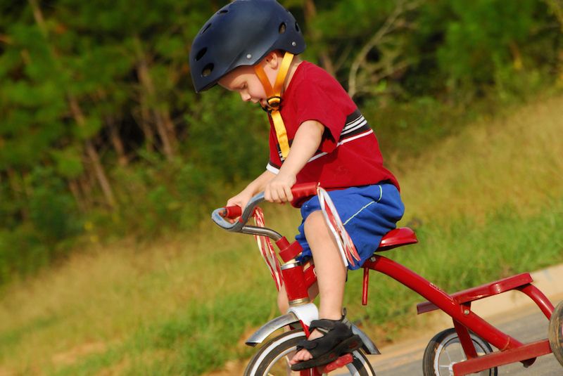 A little boy rides a tricycle, wearing a helmet