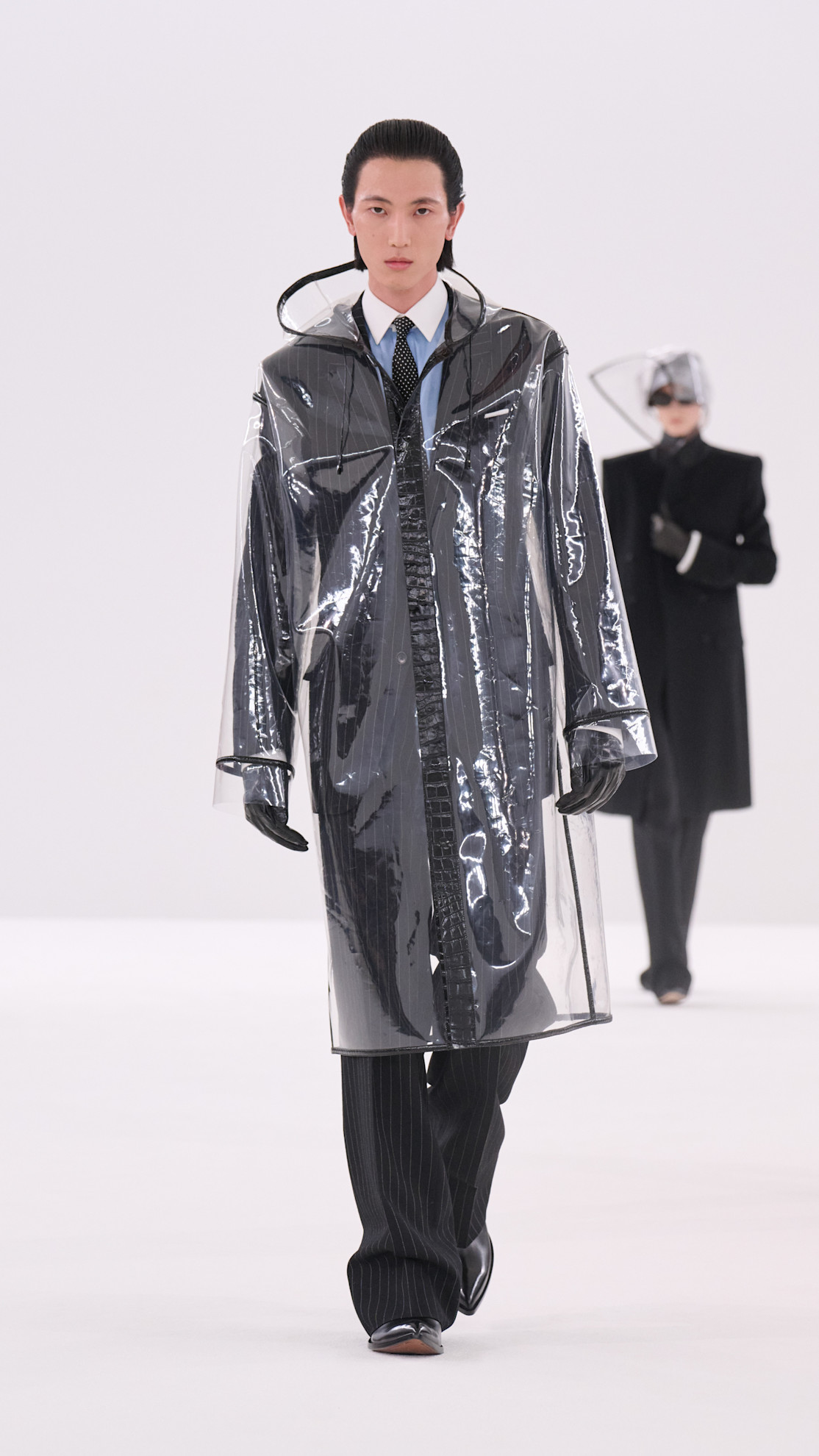 a Tom Ford model wearing a PVC coat over a pinstripe suit