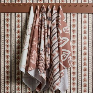 Printed tea towels from Spoonflower's collaboration with Pantone hung on wall hooks against a botanical wallpaper from the same collection featuring Pantone's colour of the year 2025, Mocha Mousse