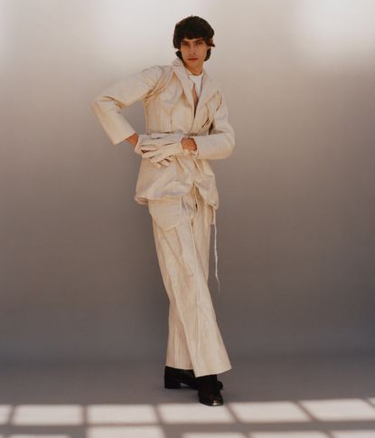 A male model wearing a cream colour blazer, gloves and trousers. 