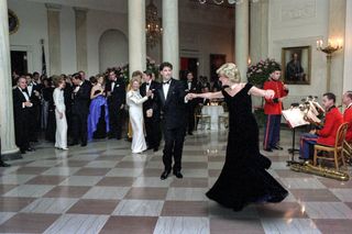 Princess Diana wearing a navy velvet gown dancing with John Travolta on a checkered floor with a band playing behind her