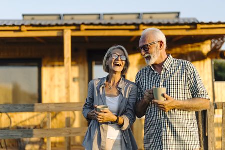 Senior couple drinking coffee and enjoying in front of the cabin house