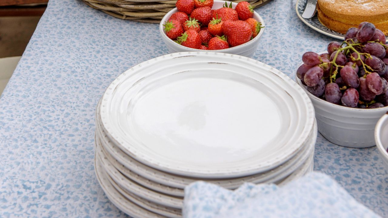 A stack of plates on an outdoor dining table with bowls of fruit