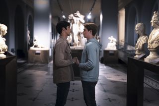 A scene from Red, White & Royal Blue showing Alex (Taylor Zakhar Perez) and Henry (Nicholas Galitzine) holding hands in the V&A Museum after-hours