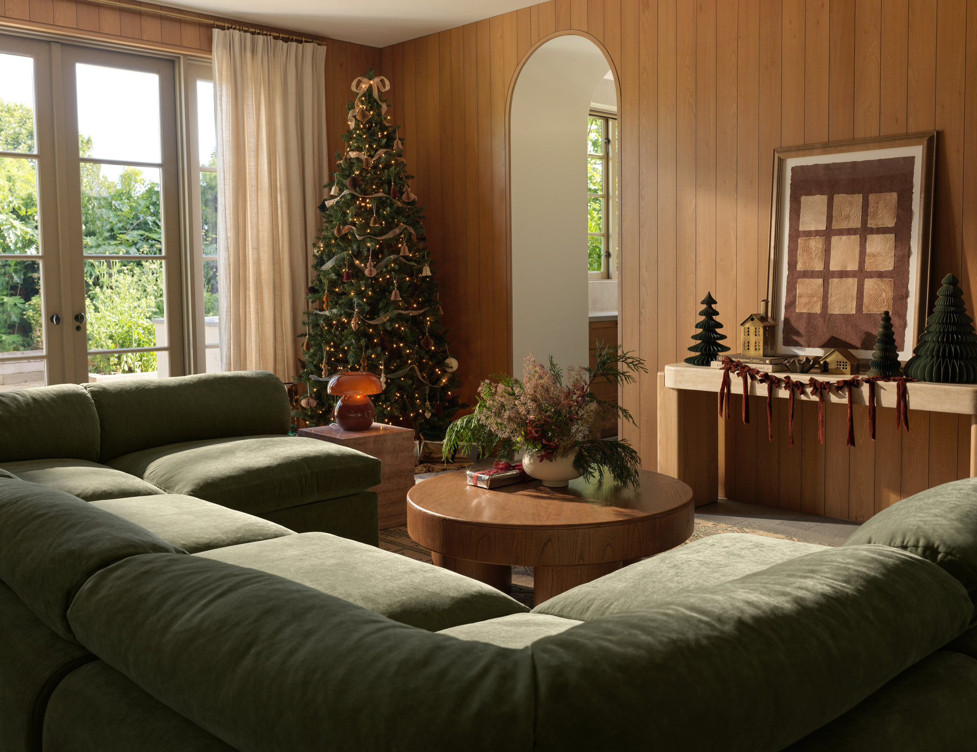 A living room with a large green sectional sofa and a Christmas tree in the corner