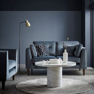 grey paneled living room with grey sofas and a white marble coffee table, accessorized with a modern steel lamp