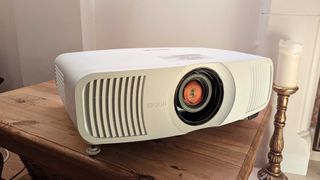 The Epson EH-LS11000W projector on a wooden table in front of a white wall